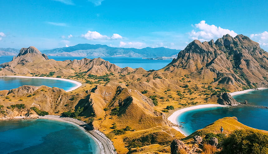 Panoramica di un isola che si apre davanti in due baie a destra e sinistra. Sulla baia di destra svettano alture semi-rocciose.