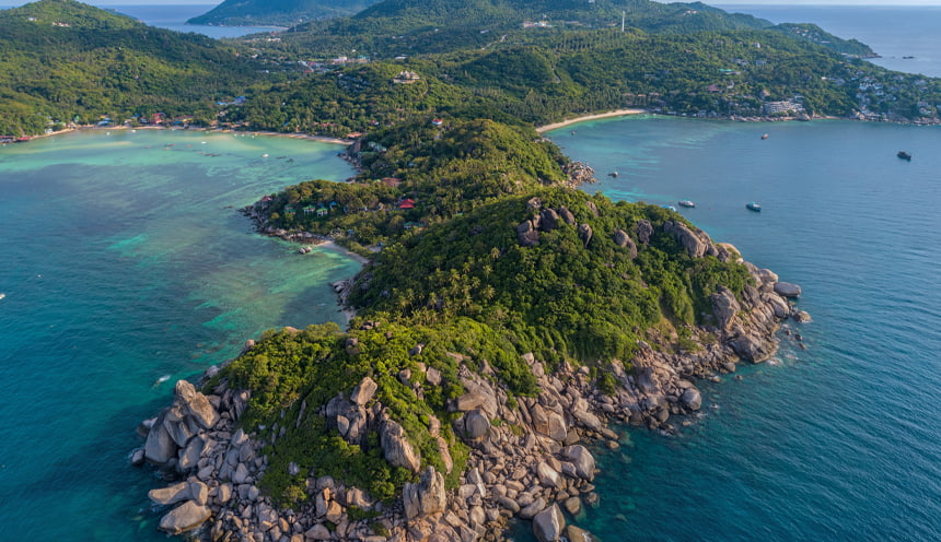 in primo piano un promontorio ricoperto da vegetazione e circondato dalle acque blu del mare in fondo a destra e sinistra si aprono due spiagge