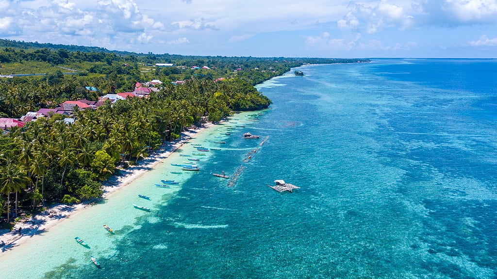 Vista aerea di una spiaggia di Wakatobi, acque turchesi, barche e il verde di palme e vegetazione tropicale sulla sinistra