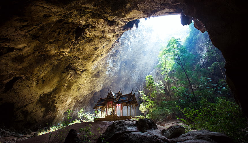 La ampia volta di una grotta e un piccolo tempio illuminato da un grosso raggio di luce solare.