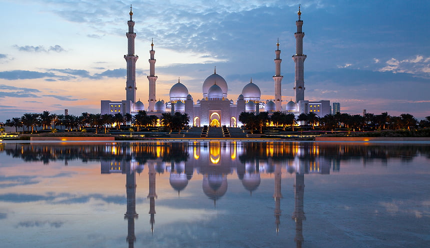 Una grande moschea durante il tramonto che si riflette nell'acqua davanti.